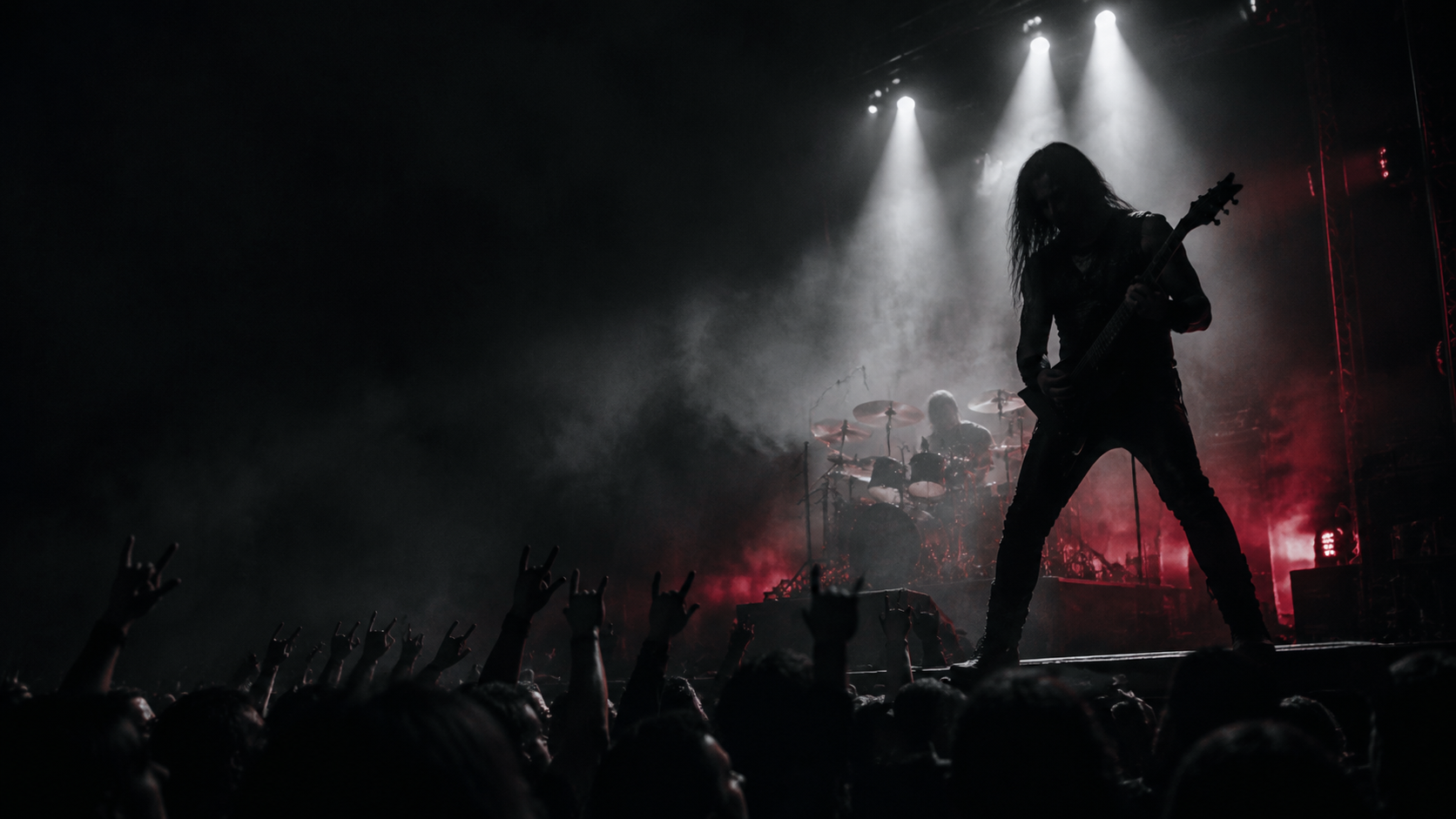 A guitarist and drummer performing on a dark stage in red and white light